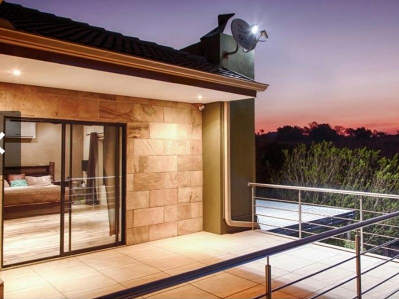 A spacious covered balcony featuring stone cladding, tiled flooring, and a modern stainless steel balustrade, offering an elevated outdoor living space.