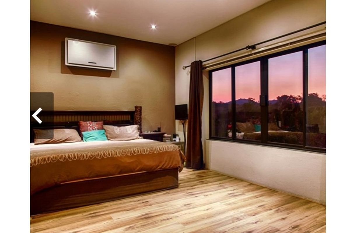 A comfortable bedroom featuring laminate wood flooring, recessed lighting, a wall-mounted air conditioning unit, and a large window offering scenic views.