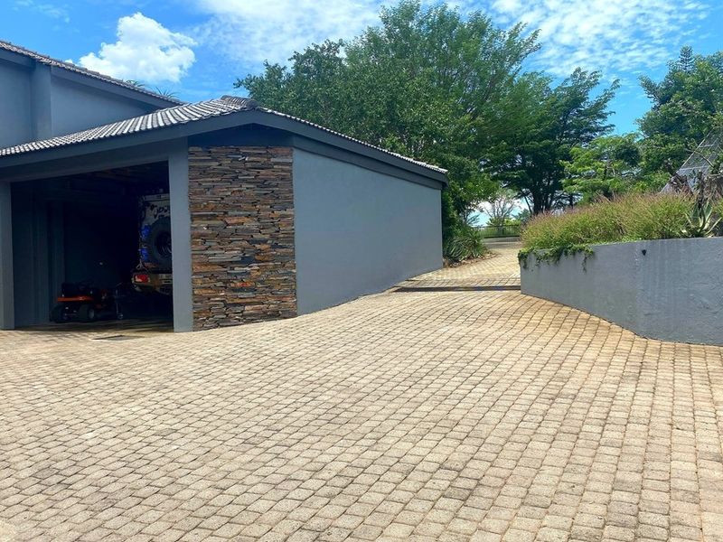 A well-maintained front exterior featuring a paved driveway, stone-clad garage facade, and a landscaped retaining wall.