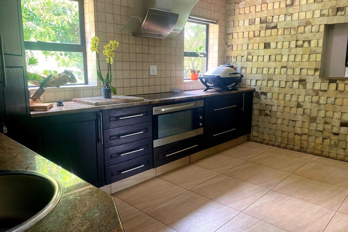 A functional kitchen featuring dark wood cabinetry, granite countertops, a built-in oven, extractor fan, and decorative tiled wall finishes.