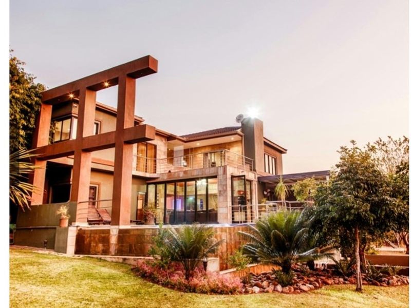 Rear view of a multi-level residence featuring stone cladding, a spacious balcony with steel railings, and large bi-fold doors opening to the garden.