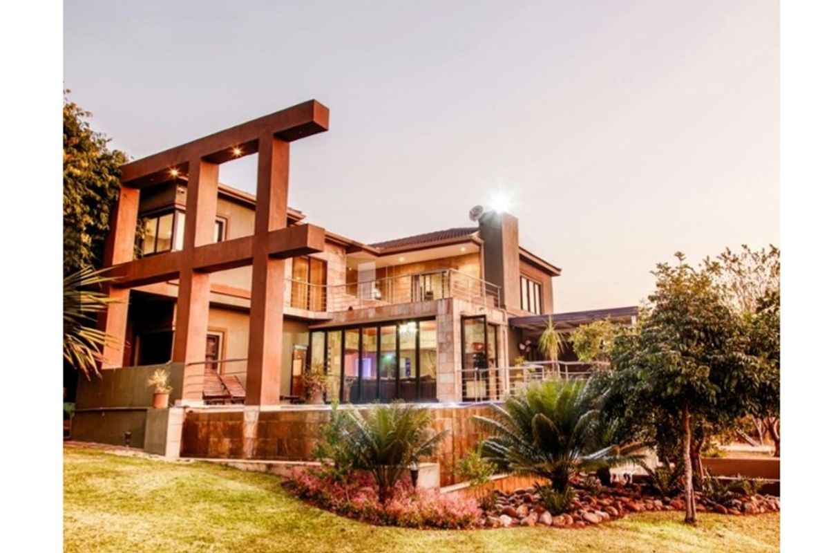 Rear view of a multi-level residence featuring stone cladding, a spacious balcony with steel railings, and large bi-fold doors opening to the garden.