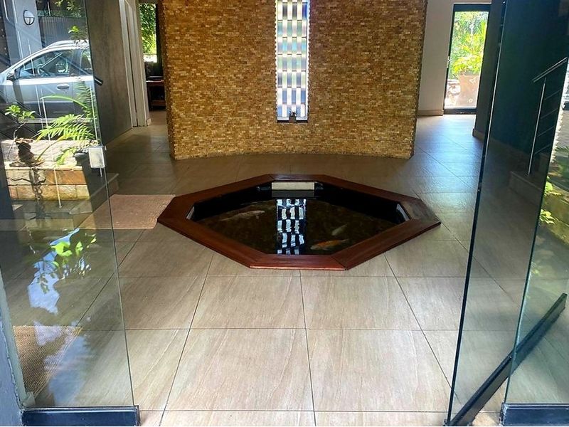Unique entrance hall featuring a built-in indoor koi pond, stone feature wall, and large glass pivot doors providing a seamless transition to the outdoors.