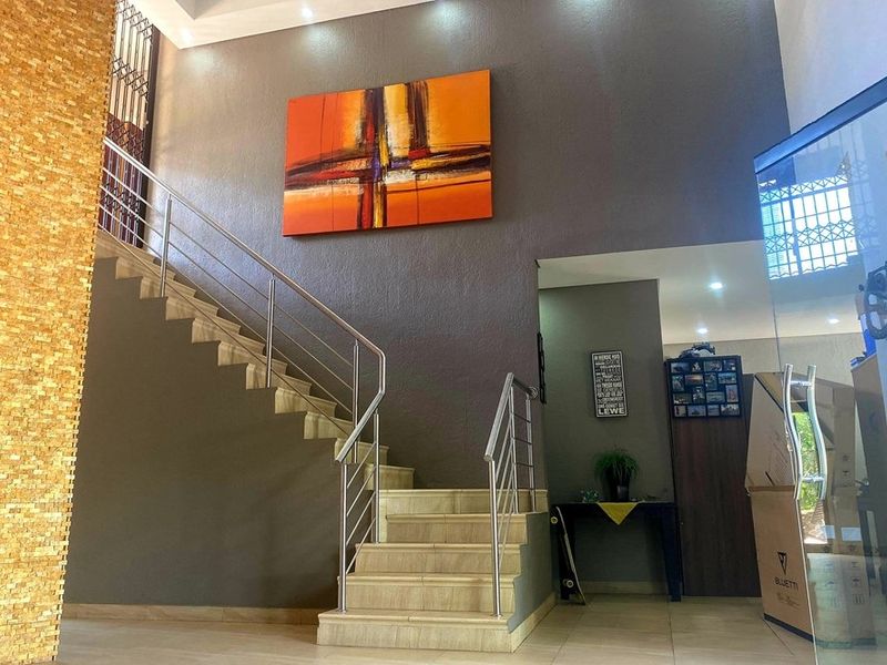Welcoming entrance hall featuring a tiled staircase with modern stainless steel balustrades and a striking mosaic feature wall.