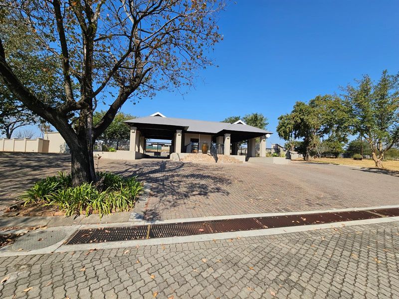 A view of the property entrance featuring a paved driveway, covered structure, and established trees in a well-maintained residential setting.