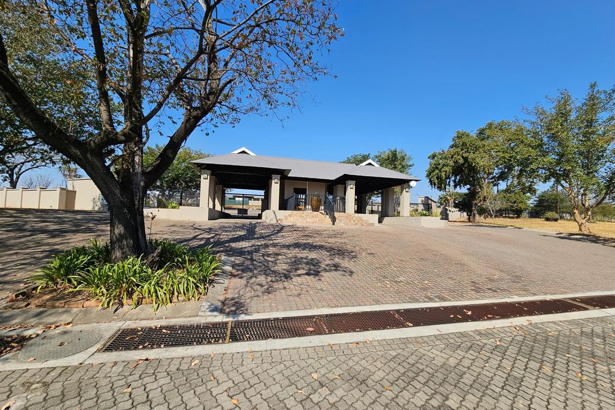 A view of the property entrance featuring a paved driveway, covered structure, and established trees in a well-maintained residential setting.