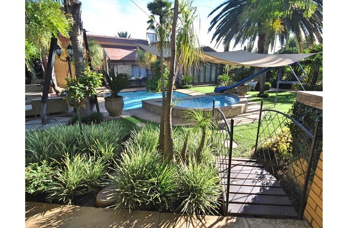 A landscaped backyard featuring a swimming pool, integrated spa, shade sail, and a decorative garden bridge, offering a private outdoor entertainment space.