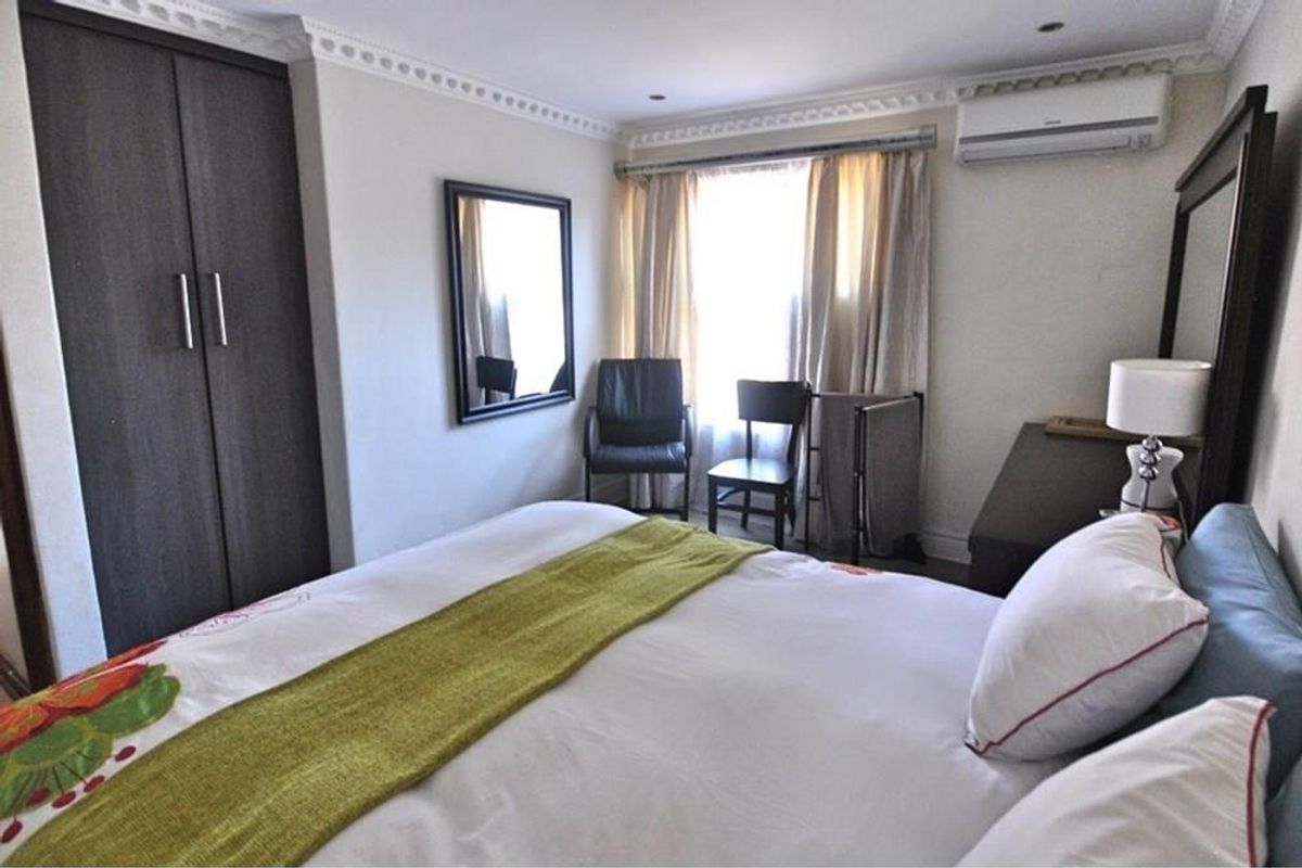 A well-lit bedroom featuring built-in cupboards, crown molding, and a wall-mounted air conditioning unit.