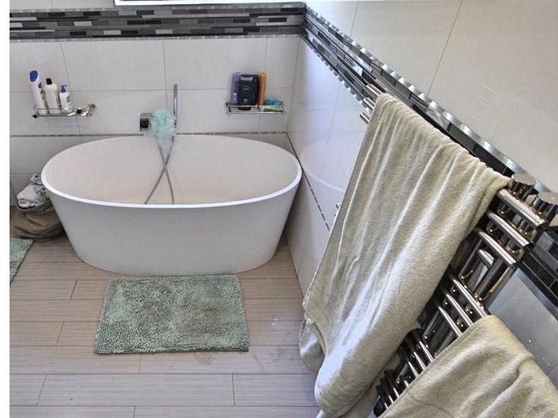 Modern bathroom featuring a freestanding oval bathtub, chrome fixtures, and a wall-mounted heated towel rail with decorative mosaic tile accents.