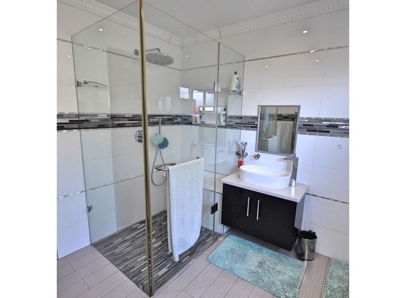 Modern bathroom featuring a glass-enclosed walk-in shower with rainfall showerhead, contemporary vanity with vessel sink, and decorative tiled wall accents.