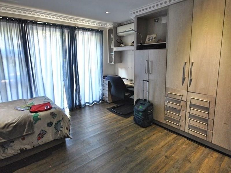 A well-appointed bedroom featuring extensive built-in cabinetry, a dedicated study nook, wood-look flooring, and sliding glass doors leading to an outdoor area.