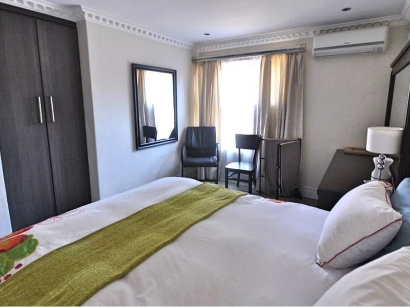 A well-lit bedroom featuring built-in cupboards, crown molding, and a wall-mounted air conditioning unit.