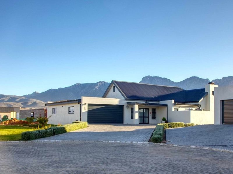 Modern residential property featuring a paved driveway, double garage, and well-maintained garden with scenic mountain views in the background.