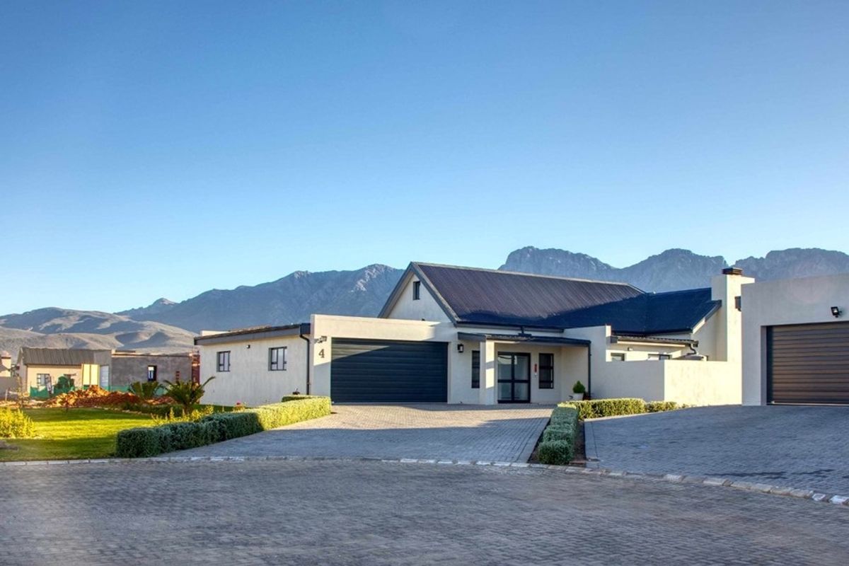 Modern residential property featuring a paved driveway, double garage, and well-maintained garden with scenic mountain views in the background.