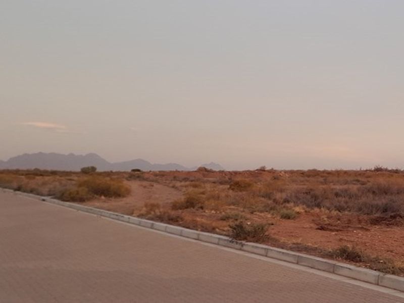 A view of a vacant residential plot featuring a paved road, concrete curbing, and distant mountain views at sunset.