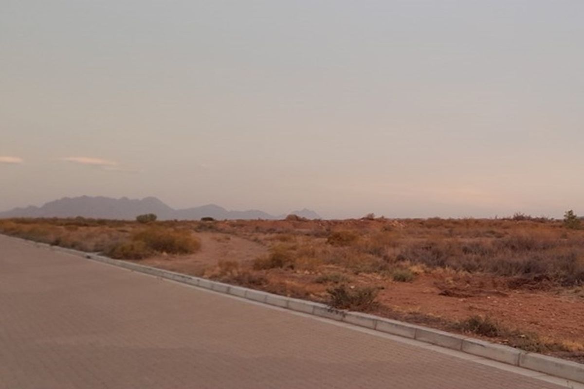 A view of a vacant residential plot featuring a paved road, concrete curbing, and distant mountain views at sunset.