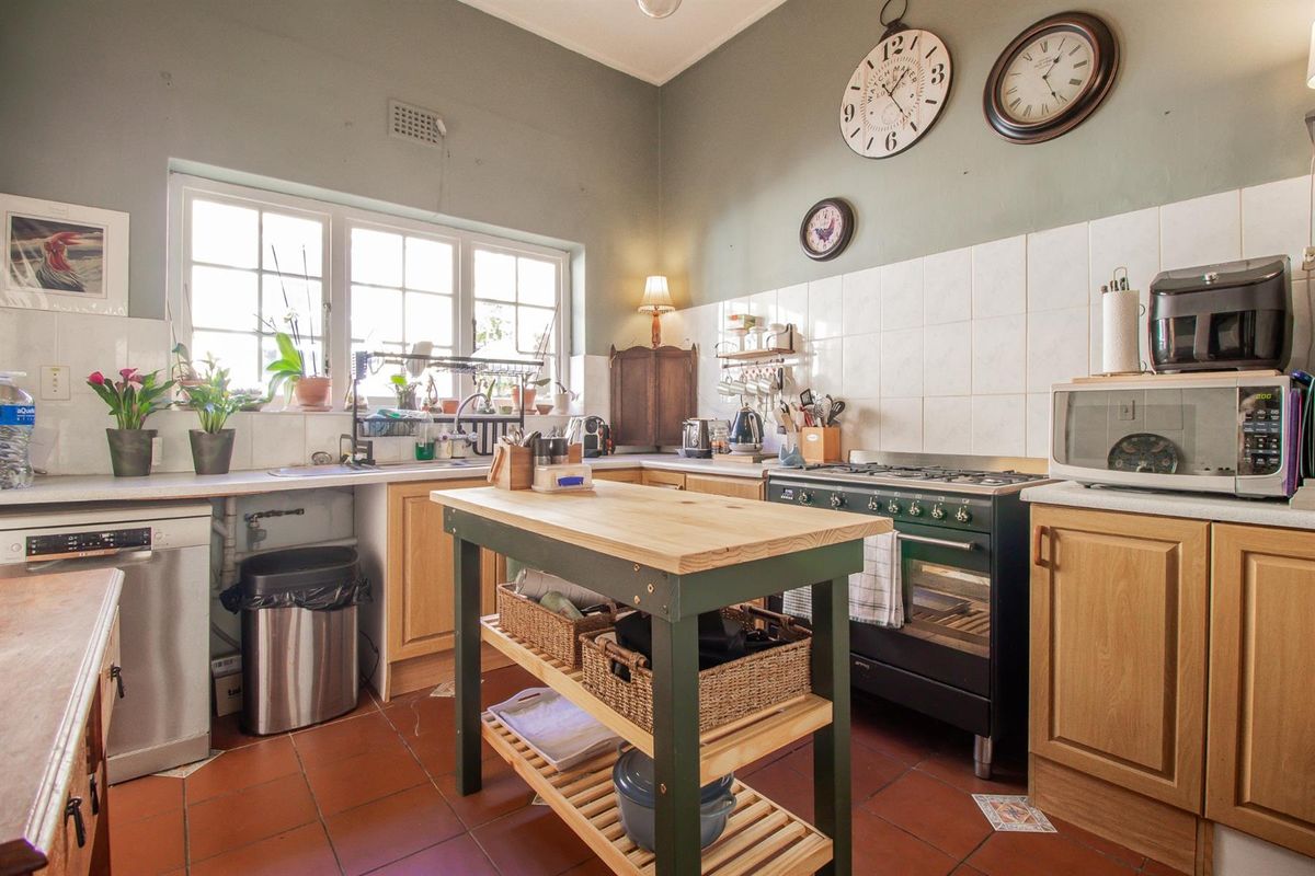 A functional kitchen featuring wooden cabinetry, a freestanding gas stove, tiled splashbacks, and terracotta floor tiles with a central prep island.