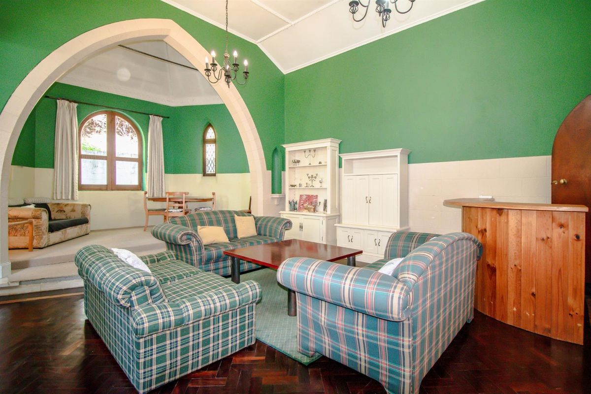 Spacious living area featuring a distinctive stone archway, vaulted ceilings, and dark parquet flooring, leading to an elevated dining space with arched windows.