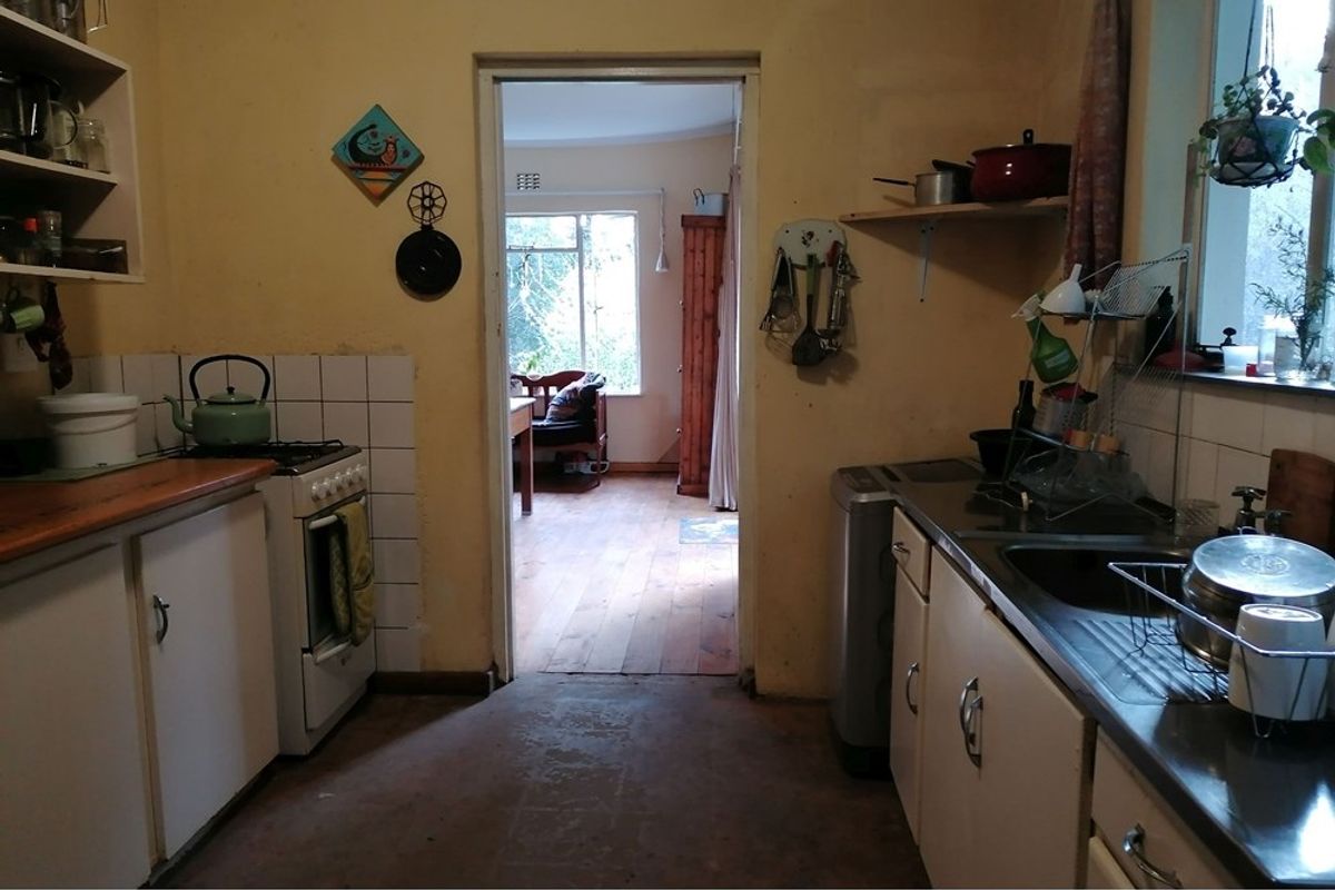 A dated kitchen featuring original cabinetry, a freestanding stove, and a stainless steel sink, with a doorway leading to an adjacent living area.