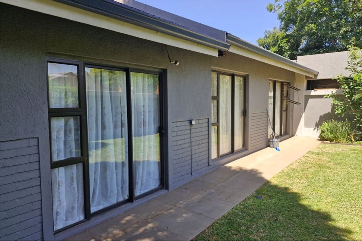 Rear exterior view of the house featuring a paved walkway, painted brick walls, and multiple sliding glass doors providing access to the garden.