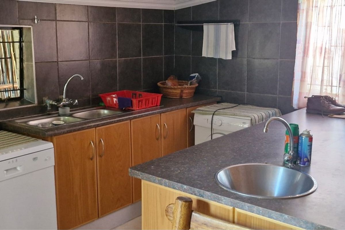 Functional kitchen featuring laminate countertops, dark tiled backsplash, double sink, and additional prep bowl with integrated cabinetry.
