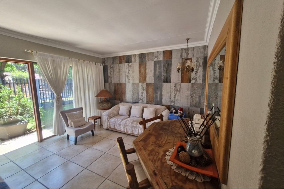 A living room featuring tiled flooring, a decorative feature wall, and a sliding glass door providing access to the garden area.