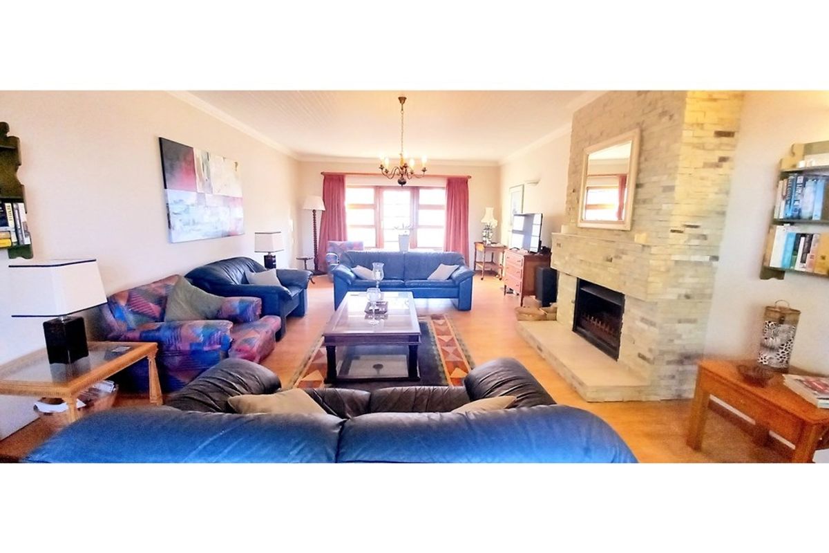 Spacious living room featuring a prominent stone-clad fireplace, wood-look flooring, and large windows allowing for natural light.