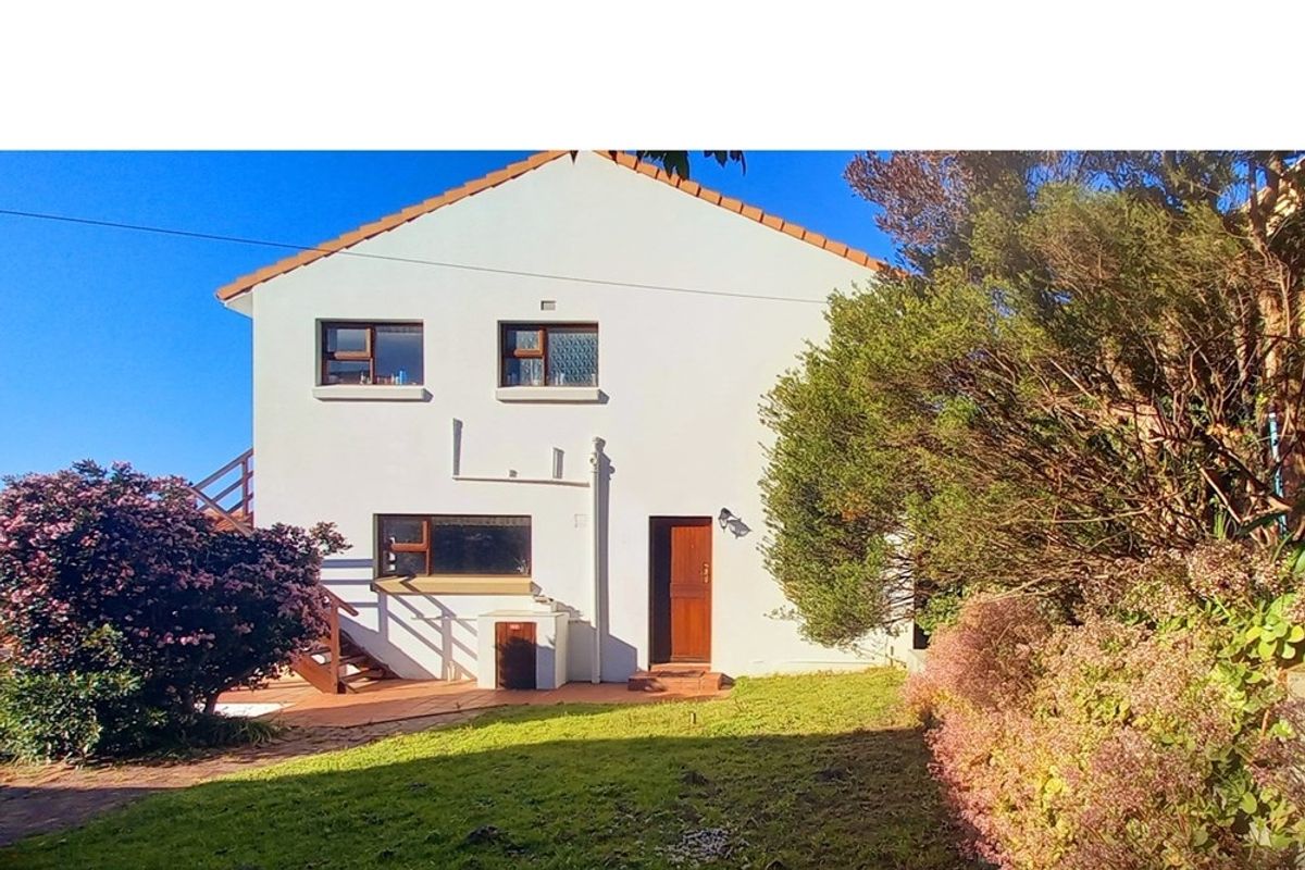 Rear view of the house featuring a tiled patio area, wooden staircase, and established garden surroundings.