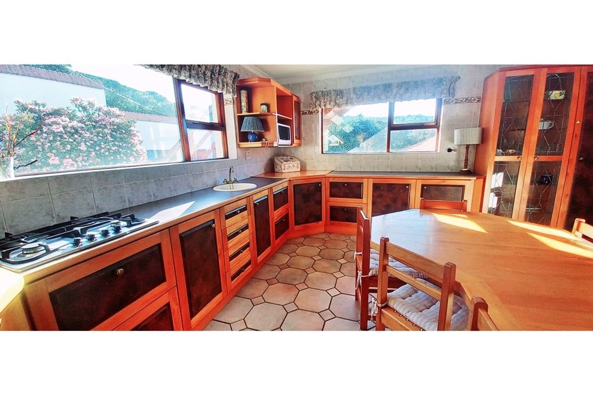 A functional kitchen featuring wooden cabinetry, tiled flooring, a built-in gas hob, and ample natural light from large windows.
