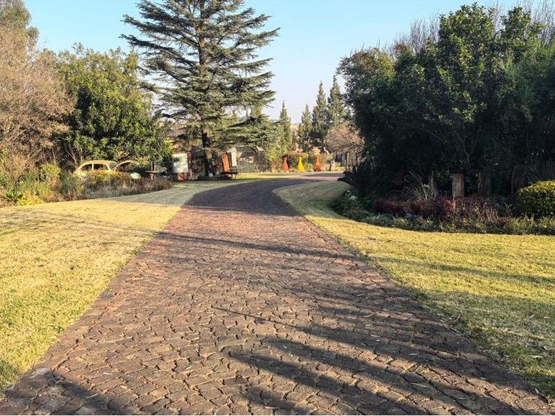 A paved driveway leading through a well-maintained garden area with mature trees and landscaped lawn.