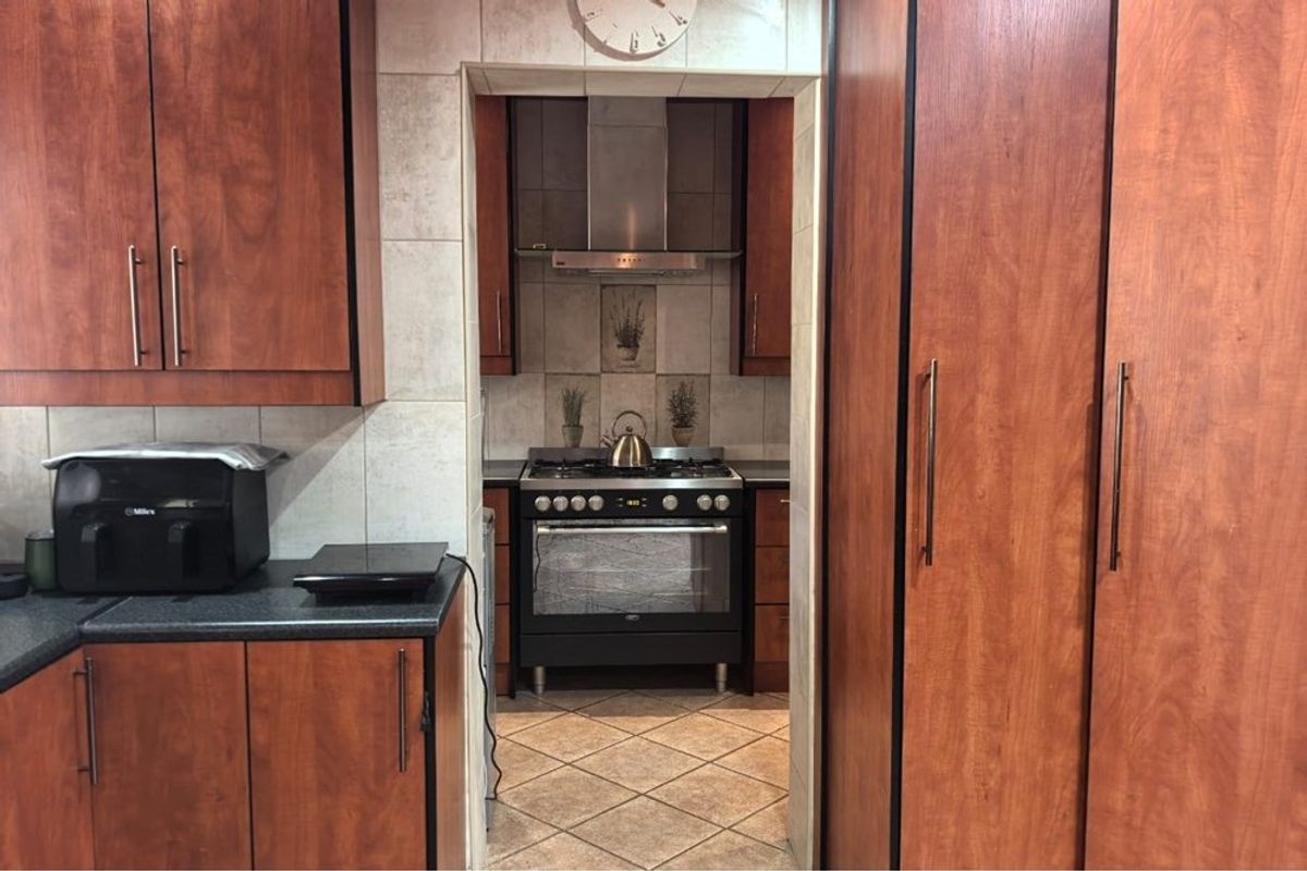 A functional kitchen featuring wood-finish cabinetry, tiled splashbacks, and a built-in oven with a stainless steel extractor fan.