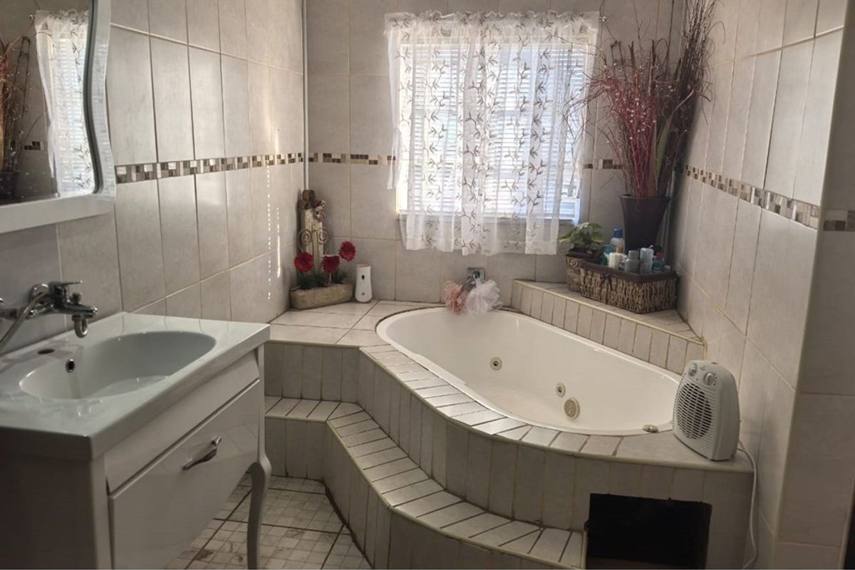A bathroom featuring a built-in corner jetted bathtub with tiled steps and a vanity basin with wall-mounted faucet.
