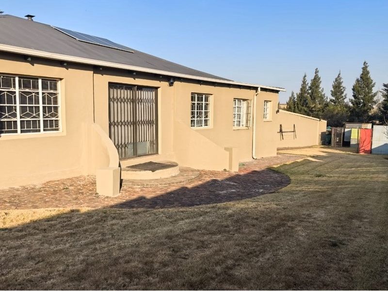 Rear view of the apartment featuring a paved patio area, security gates on sliding doors, and a spacious private garden.