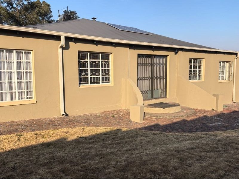 Rear view of the property featuring a paved patio area, metal security gate, and solar panels installed on the roof.