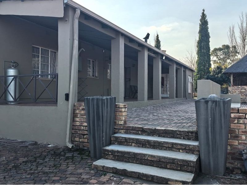 A spacious covered patio area featuring brick paving, concrete steps, and a structural veranda overlooking the rear garden space.