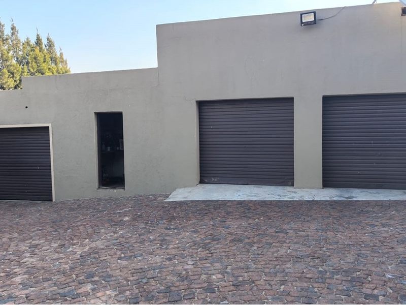 Exterior view of a multi-car garage featuring three roller shutter doors and a paved driveway area.