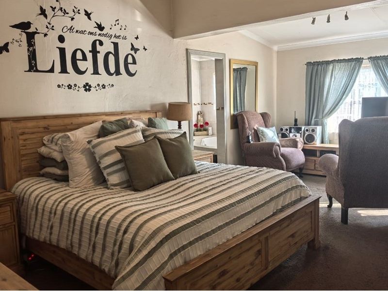 Spacious bedroom featuring an en-suite bathroom access, neutral wall tones, and large windows allowing for natural light.