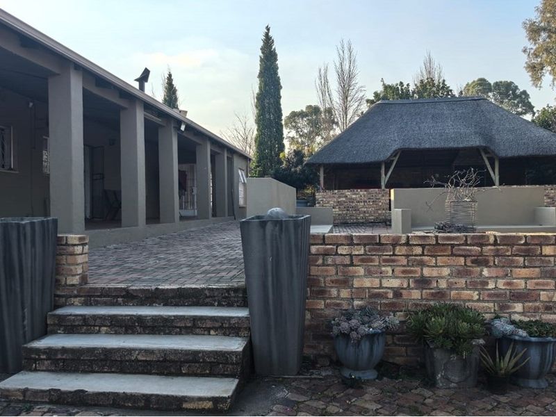 Outdoor patio area featuring a covered walkway, brick paving, and a separate thatched lapa structure in the garden.