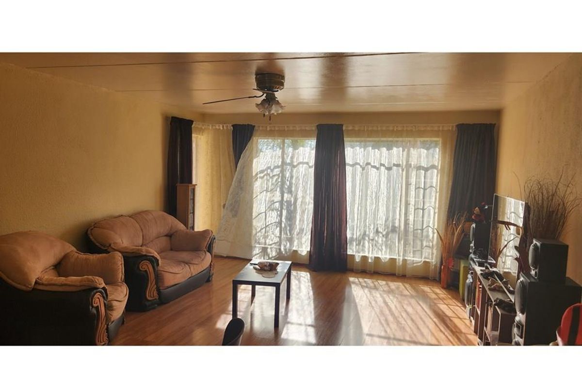 A living room featuring wood-look flooring, a ceiling fan, and large windows that provide natural light.