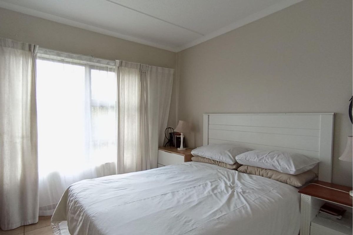 A bright and neutral bedroom featuring large windows with natural light, providing a comfortable and airy living space.