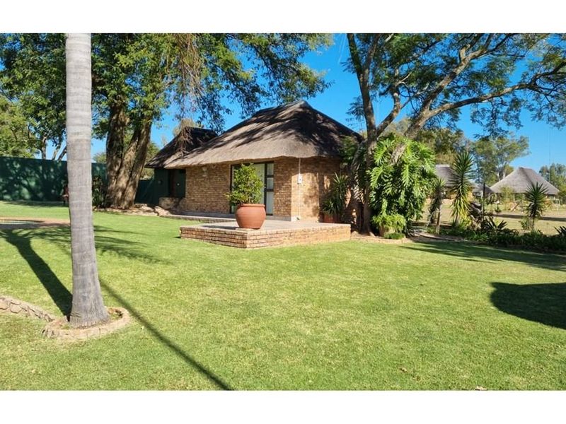 A view of the rear garden featuring a brick-built structure with a traditional thatched roof and a paved patio area.