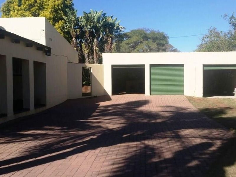 Exterior view of the property featuring a paved driveway leading to a multi-car garage with roller doors and adjacent building structure.