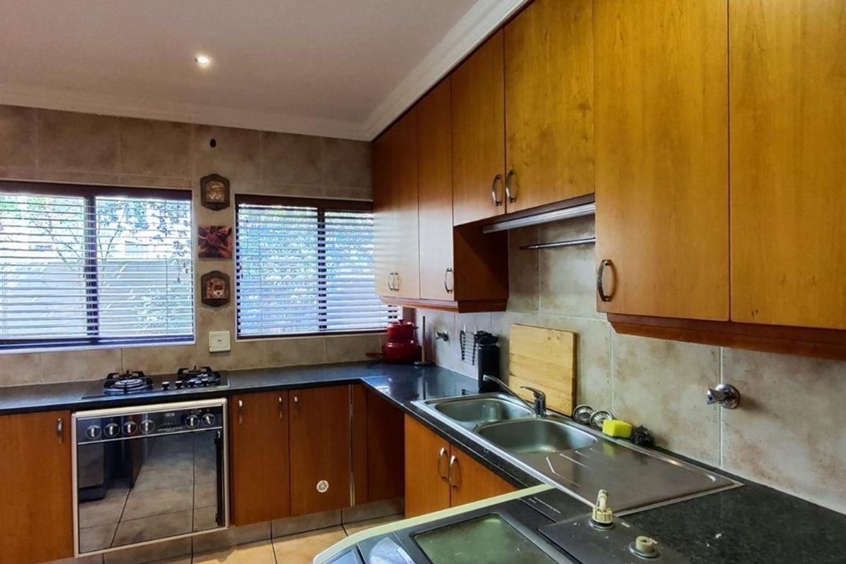 A functional kitchen featuring wooden cabinetry, dark countertops, a built-in gas hob, oven, and a double stainless steel sink with tiled splashbacks.