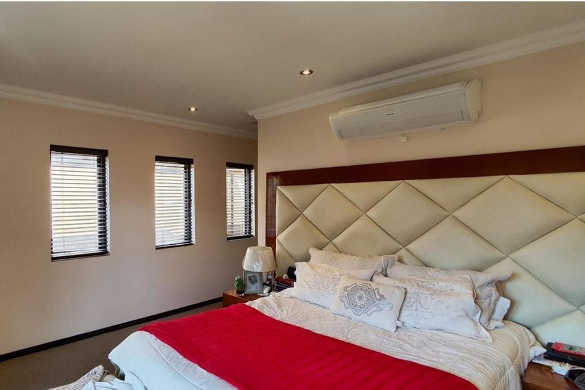 A well-maintained bedroom featuring a large upholstered headboard, recessed ceiling lighting, and a wall-mounted air conditioning unit.