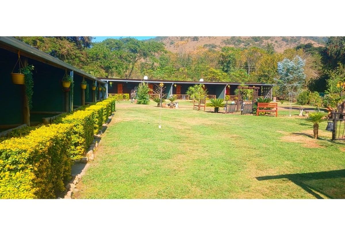 A view of the lodge exterior featuring a well-maintained lawn, landscaped garden, and a covered patio area extending along the building facade.