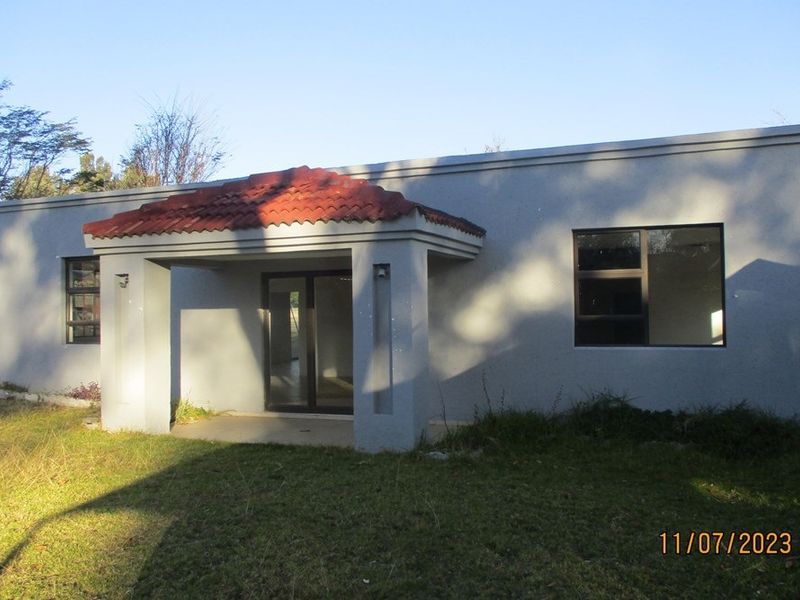 Rear view of the residential property featuring a covered patio entrance, sliding glass doors, and aluminium window frames set against a grassed yard.