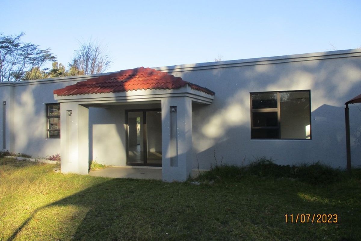 Rear view of the residential property featuring a covered patio entrance, sliding glass doors, and aluminium window frames set against a grassed yard.