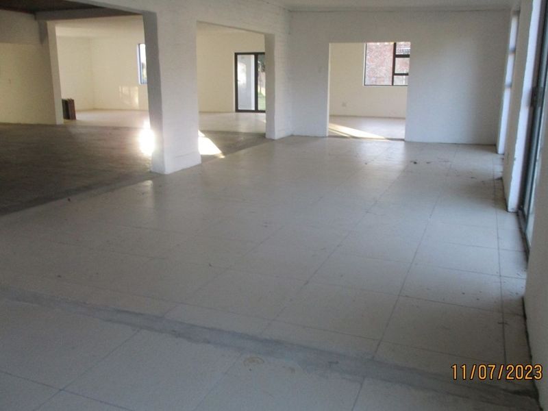 Spacious open-plan living area featuring tiled flooring, structural columns, and large sliding glass doors, offering a blank canvas for renovation.