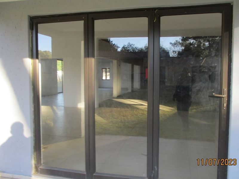 View through large aluminium sliding doors into an open-plan interior space, showing tiled flooring and neutral wall finishes.