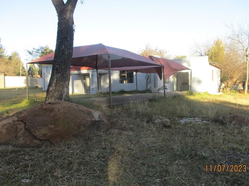 Rear view of the residential property featuring a concrete patio area with a shade sail, set within a large, overgrown garden plot.